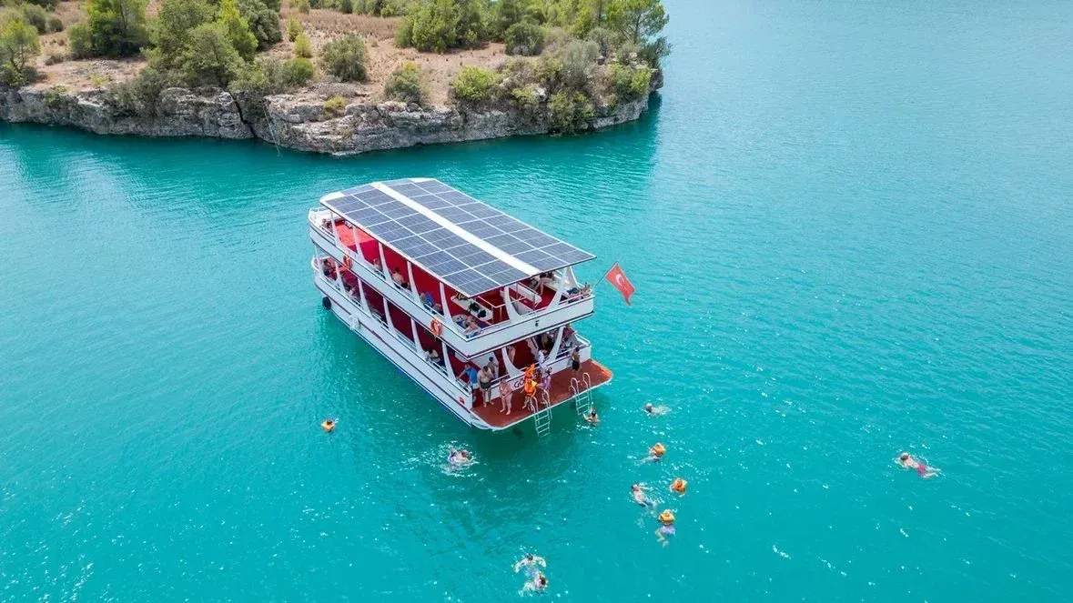 Badende rund um die Plattform eines Doppeldeck-Boots auf dem türkisfarbenen Wasser des Oymapınar-Stausees
