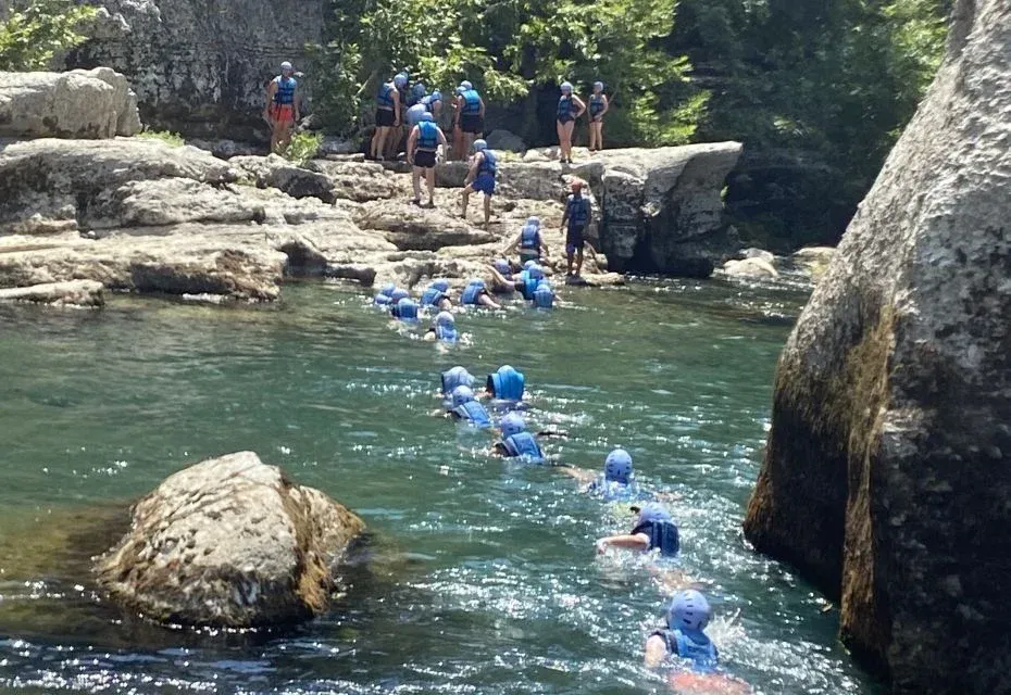 Eine Gruppe mit Helmen und Schwimmwesten treibt durch den grünen Köprüçay zwischen Kalksteinblöcken