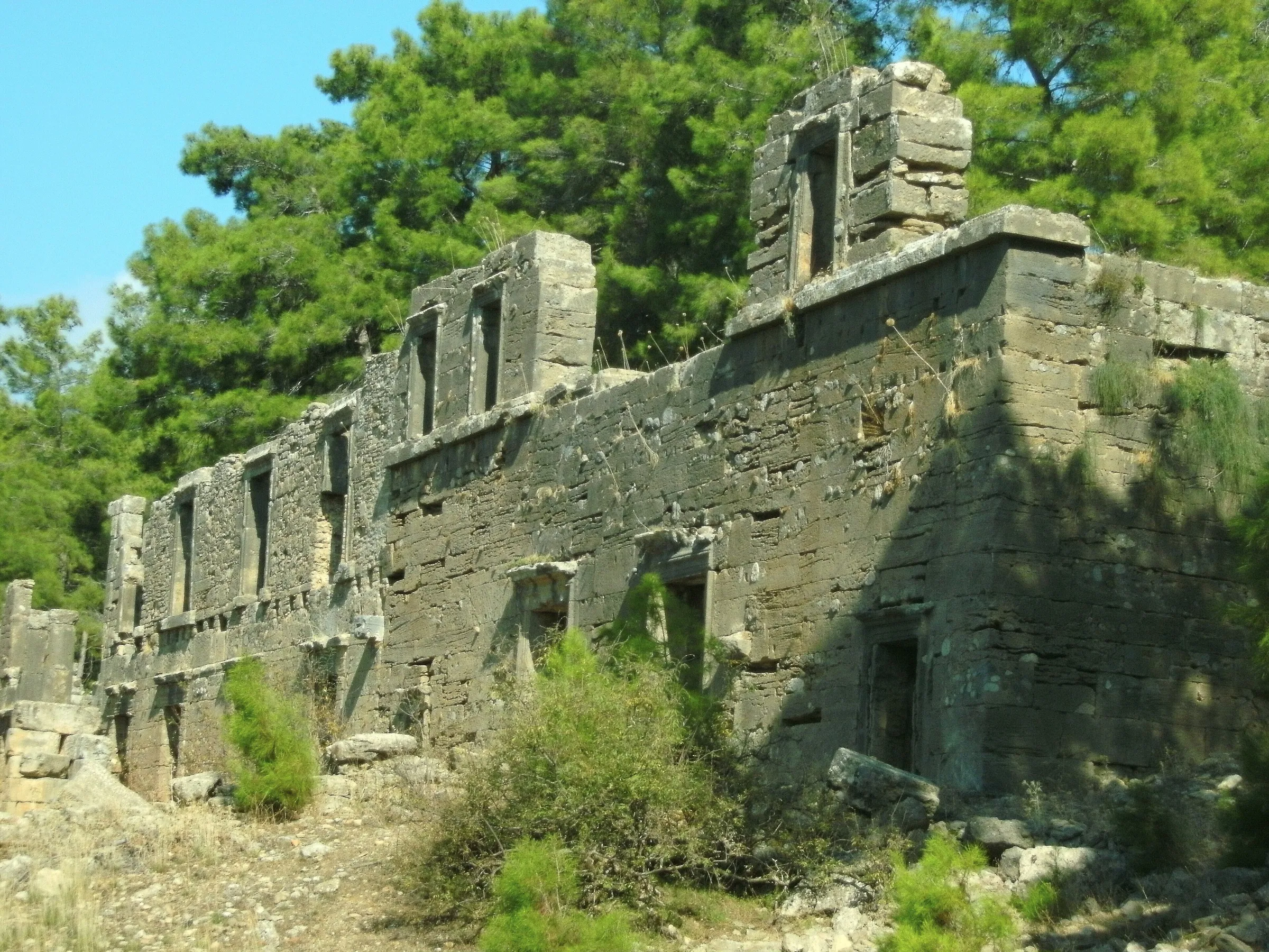 Die zweigeschossige Ladenfassade der Agora von Seleukeia (Lyrbe) mit erhaltenen Tür- und Fensteröffnungen, dahinter Kiefernwald