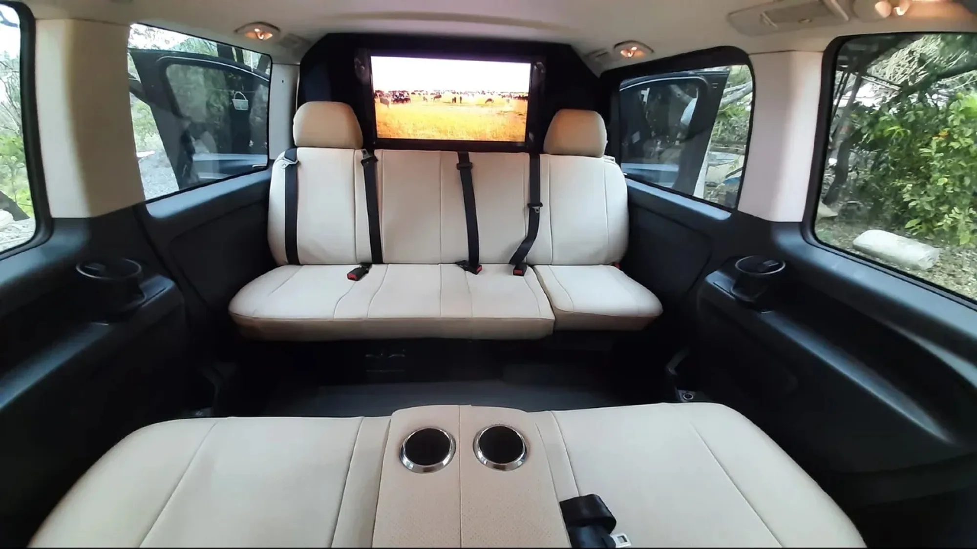 Empty rear bench of a private transfer minivan, cream leather seats and a wide window